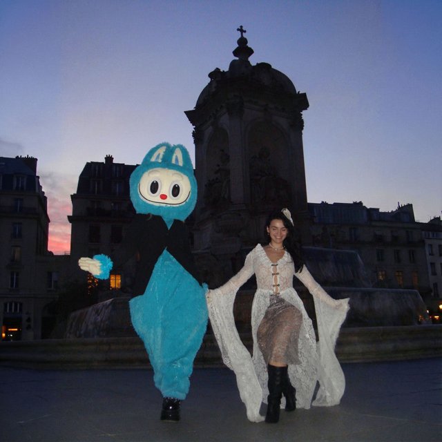 Pochette de Is It a Crime ? : une femme en robe blanche à côté d’un personnage costumé bleu, devant un bâtiment à dôme au crépuscule