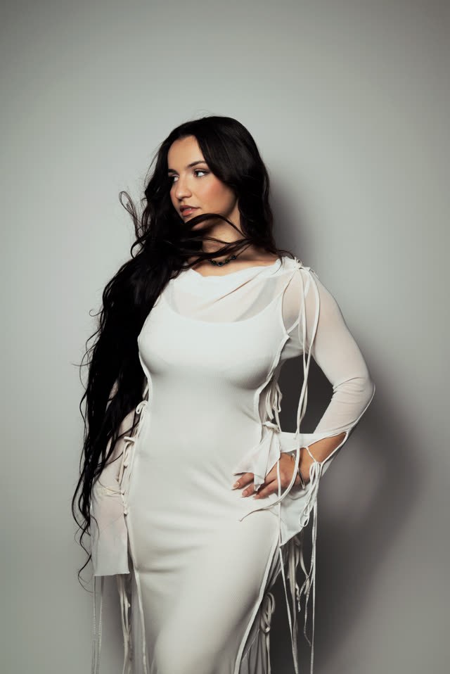 Myla en robe blanche sur fond gris, la main sur la hanche
