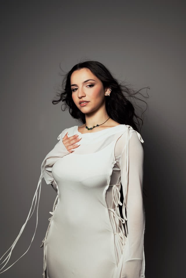Myla en robe blanche sur fond gris, les cheveux en mouvement
