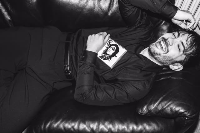 Rosenfeld allongé sur un canapé en cuir noir, une pochette de disque à la main
