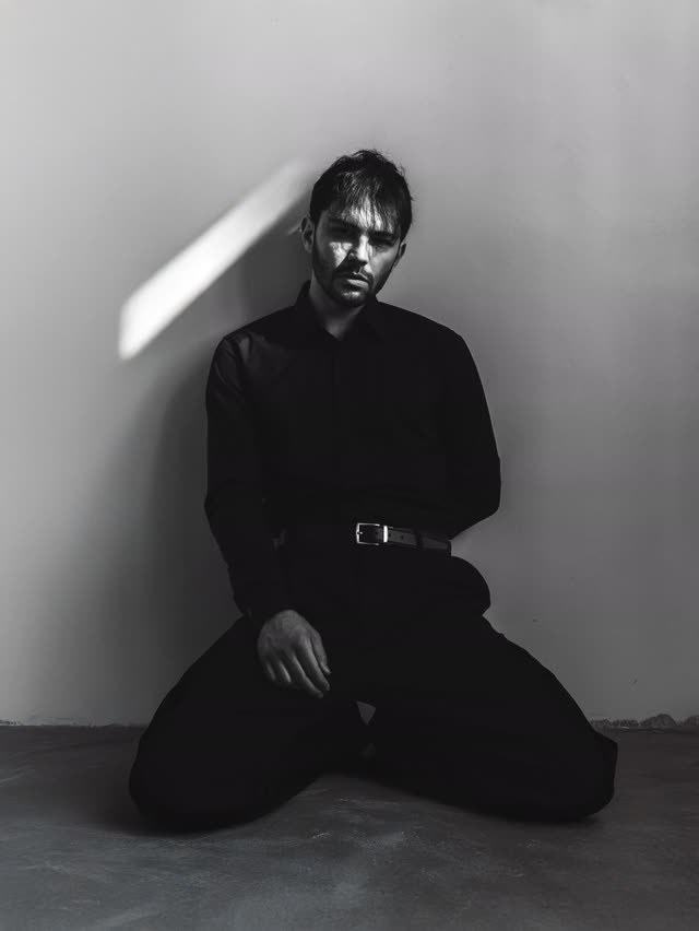 Rosenfeld en noir, à genoux dans une pièce nue