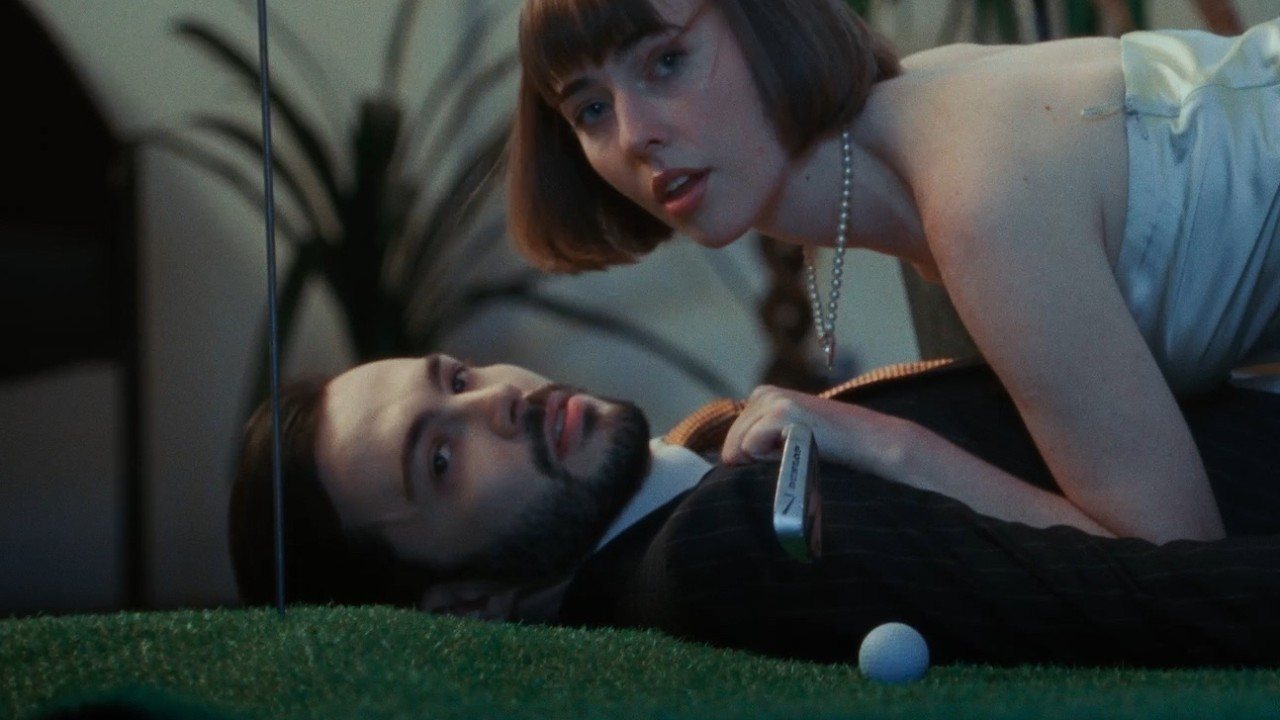 Une scène du clip de Undressed : une femme penchée sur un homme allongé sur un gazon artificiel, près d’une balle de golf